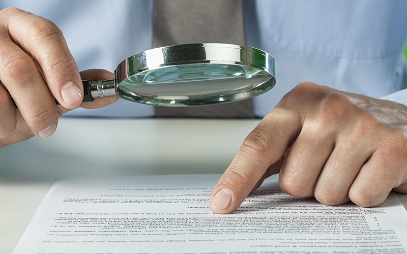 Picture of man holding magnifying glass over document